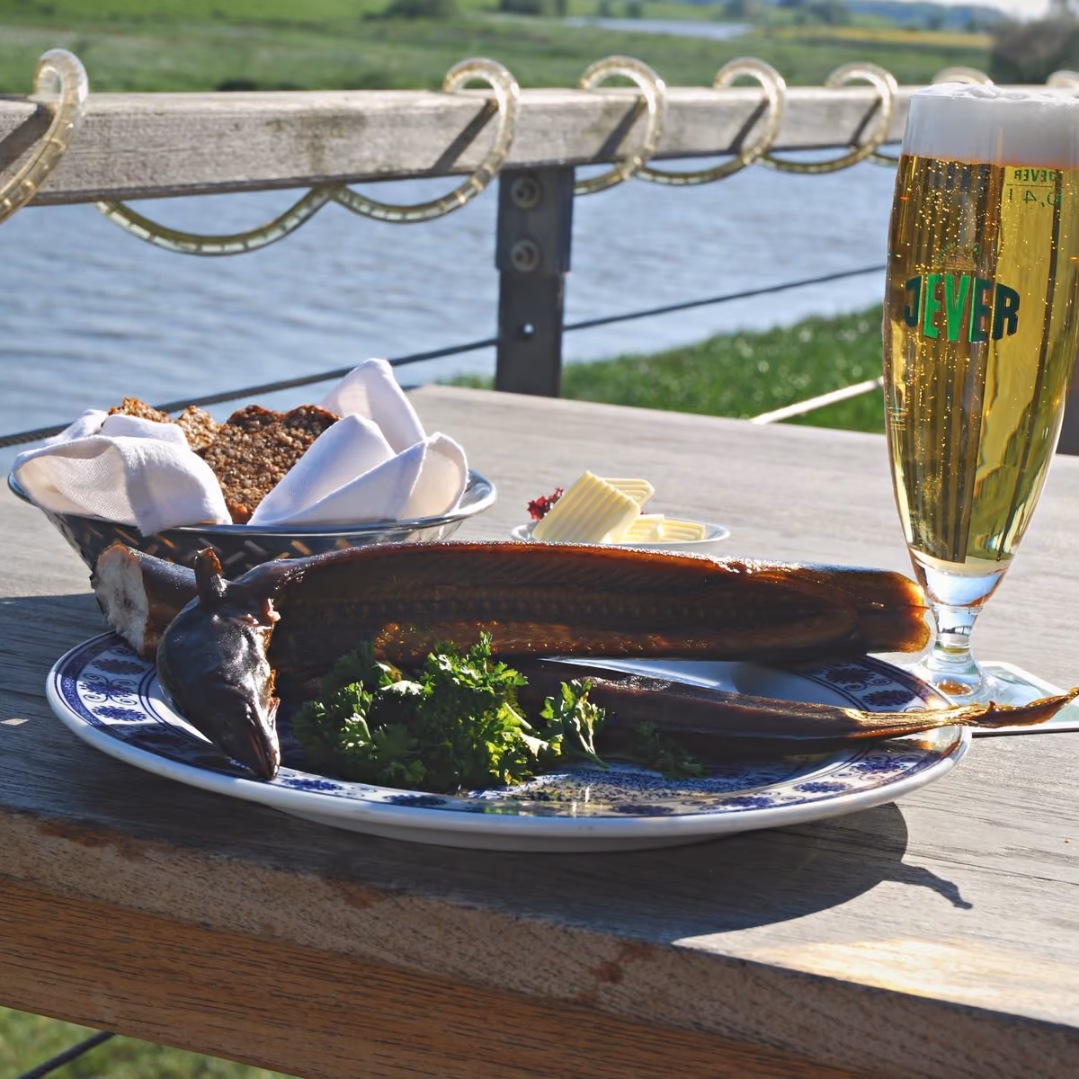 Kuchen und ein Glas Sekt auf einem Tisch am Steg, dahinter das Wasser