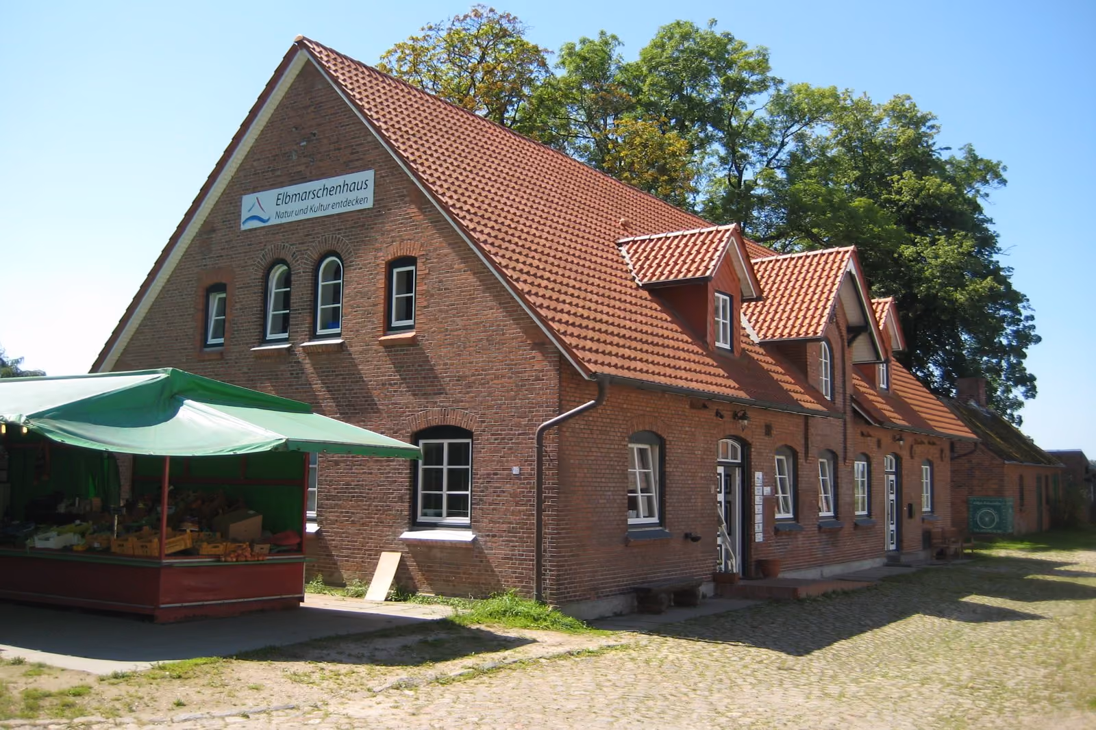 Das Elbmarschenhaus in Haseldorf, ein langes Backsteinhaus mit grüner Markise